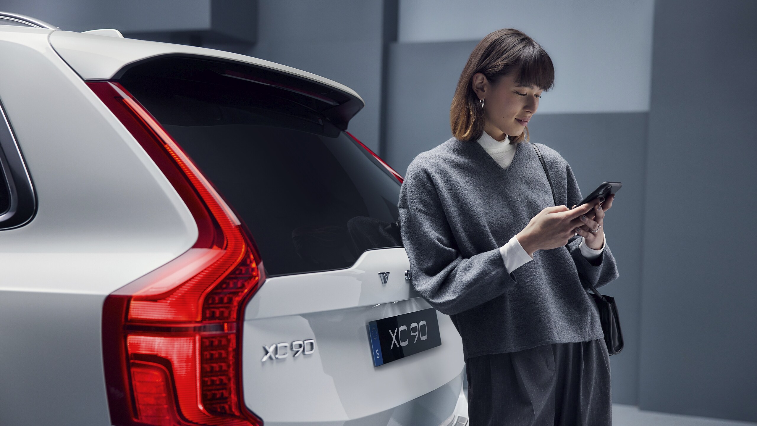 Una mujer recargada en un Volvo XC90 sosteniendo su celular