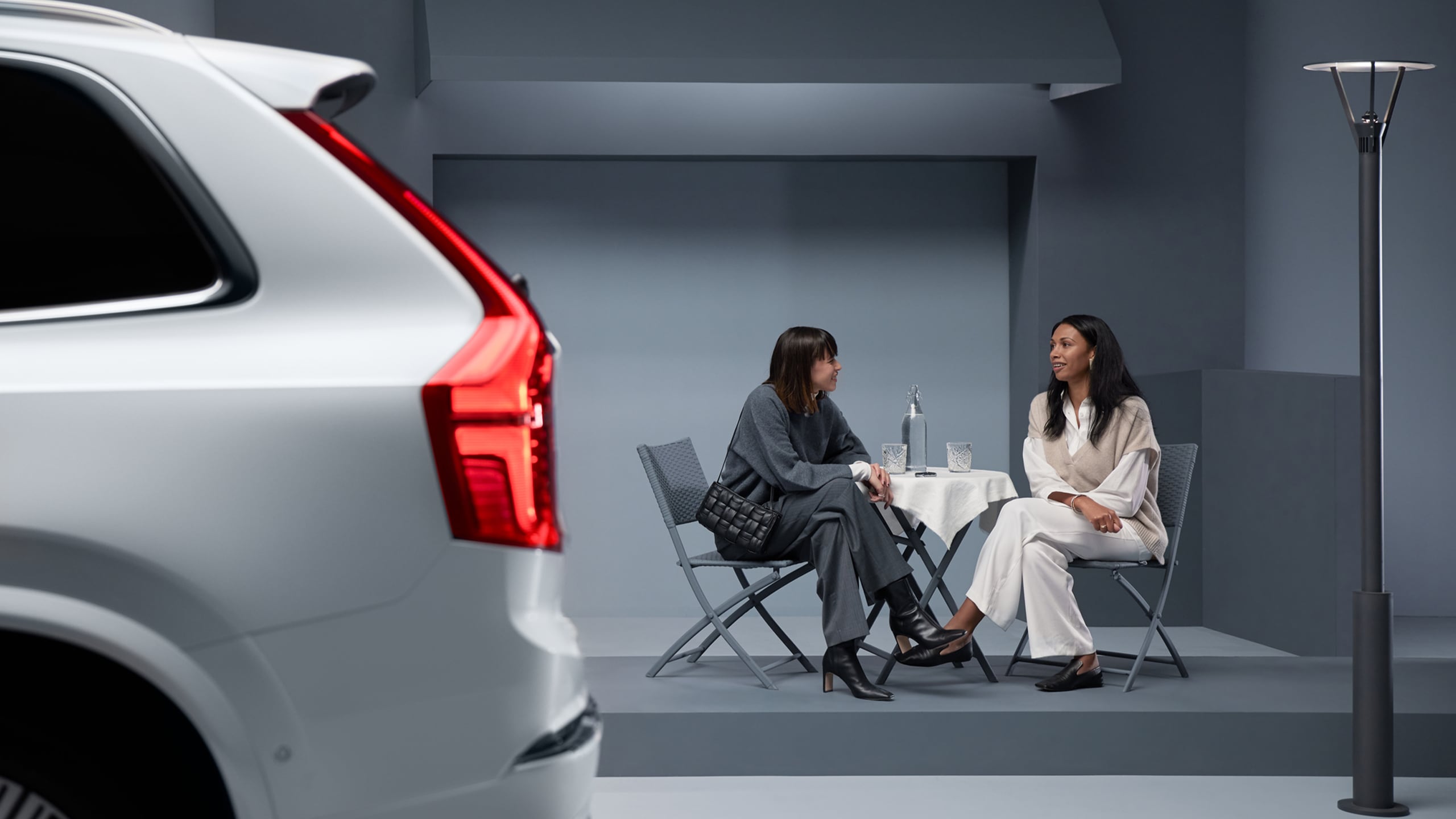 La esquina trasera de un Volvo con dos mujeres al fondo sentadas platicando.