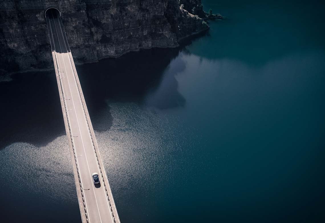 A Volvo driving over a body of water on a long two lane bridge