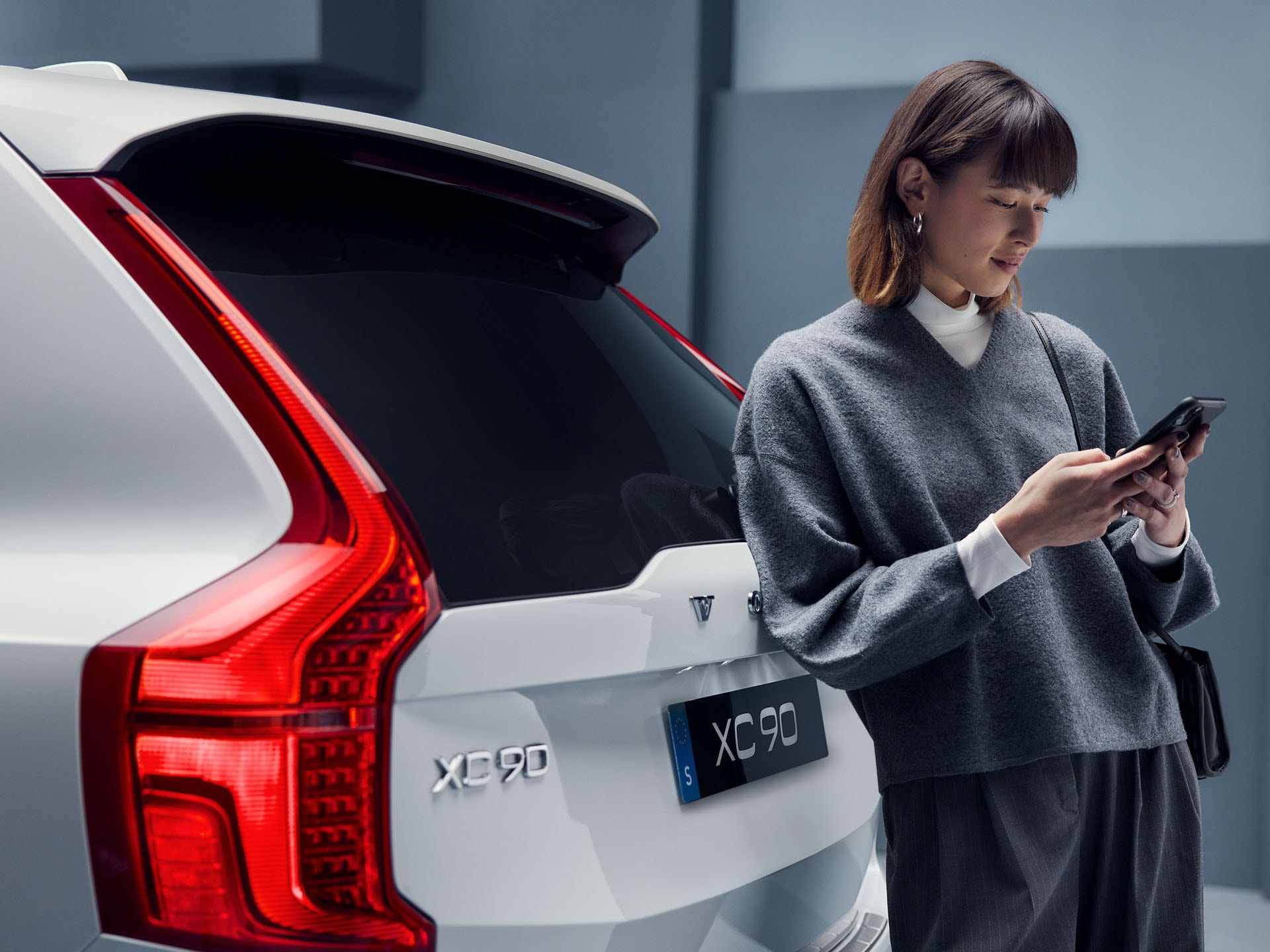 Volvo XC90 y una mujer apoyada en la parte trasera mientras habla por teléfono