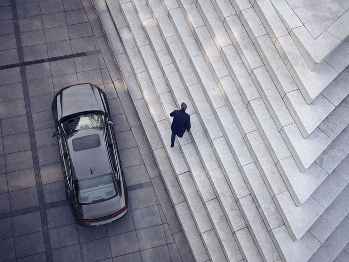 Un hombre subiendo las escaleras y un Volvo S90 aparcado