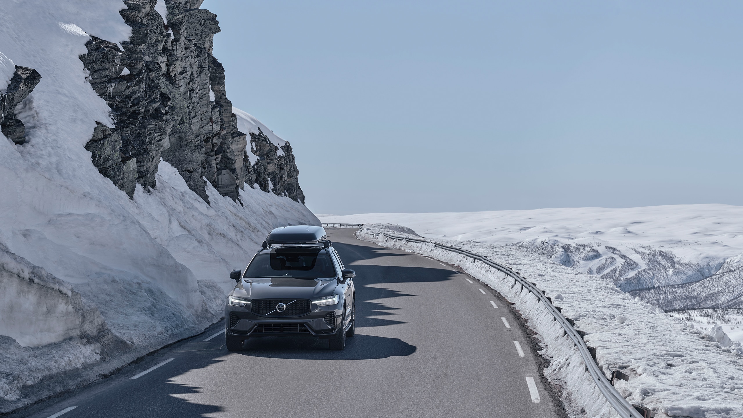 Svart Volvo XC60 Recharge kör på snötäckt bergsväg