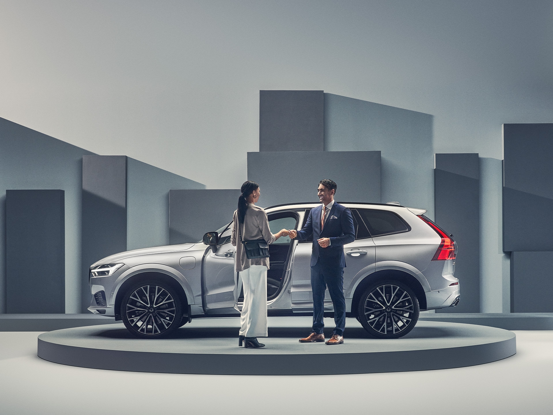 Man and woman standing next to a bright silver metallic XC60 Recharge T8 AWD in a studio setting.