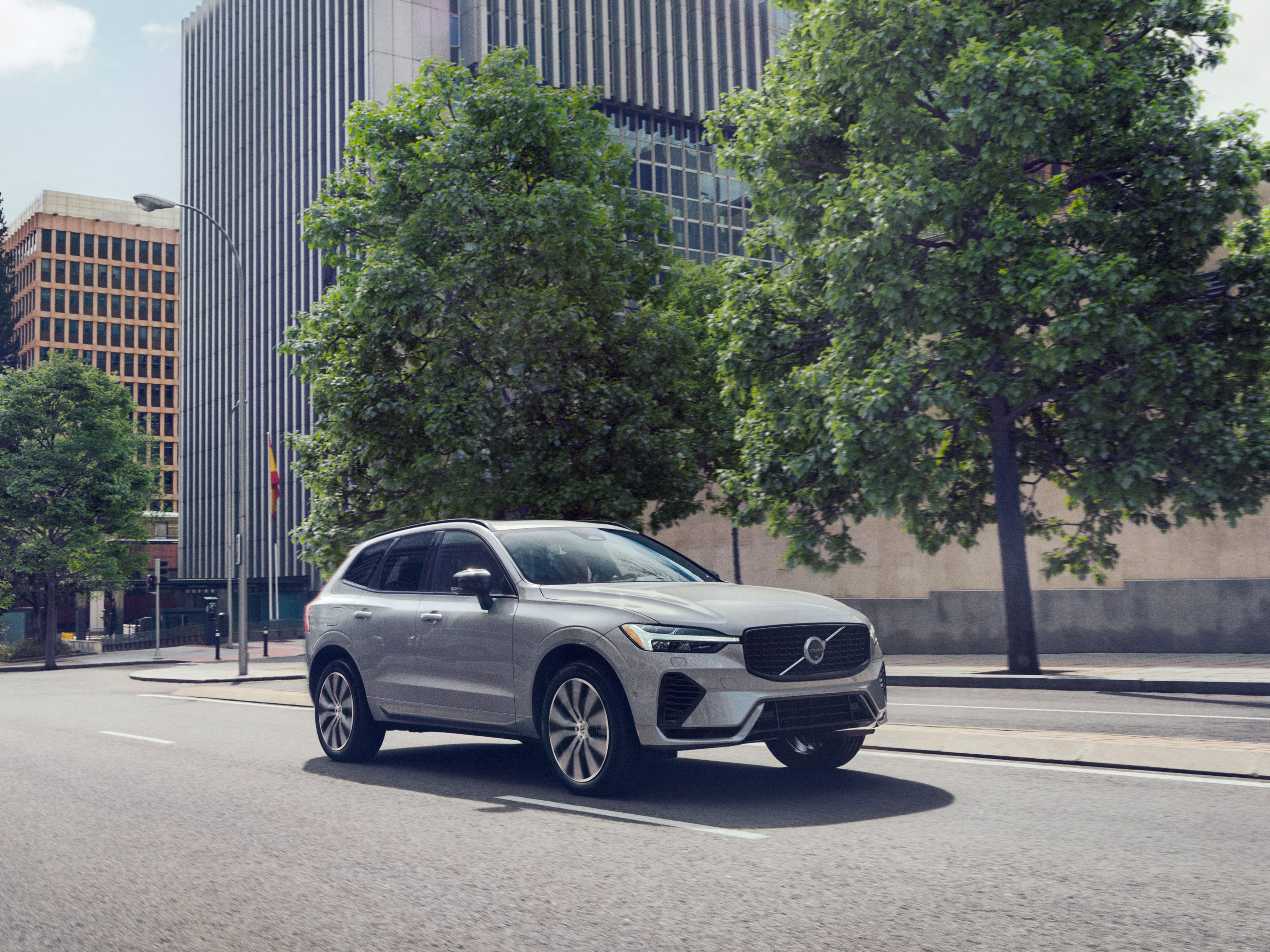 A Volvo XC60 Recharge plug-in hybrid driving in an urban environment with trees in the background.