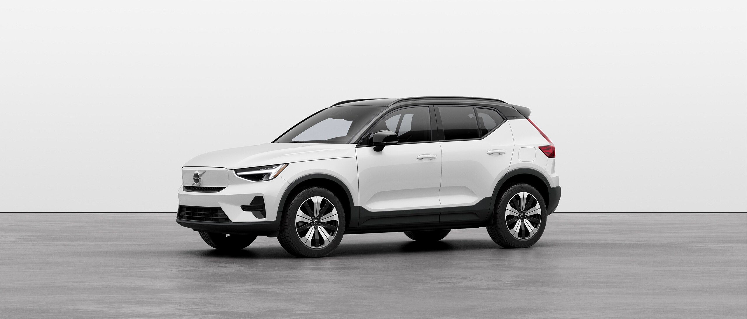 A white Volvo XC40 Recharge SUV standing still on grey floor in a studio.