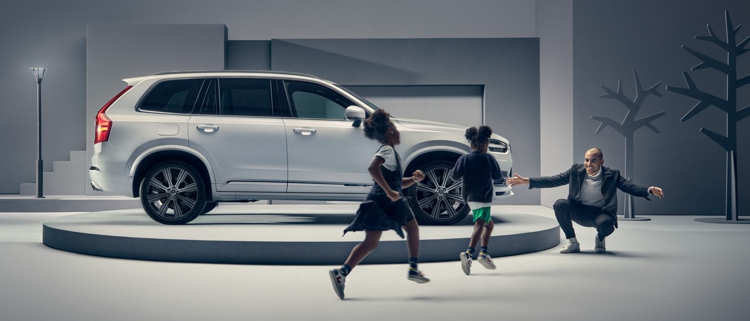 A man greets two children in front of a Volvo on a podium.