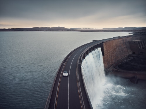 Volvo SUV drives on a bridge that crosses a water reservoir.