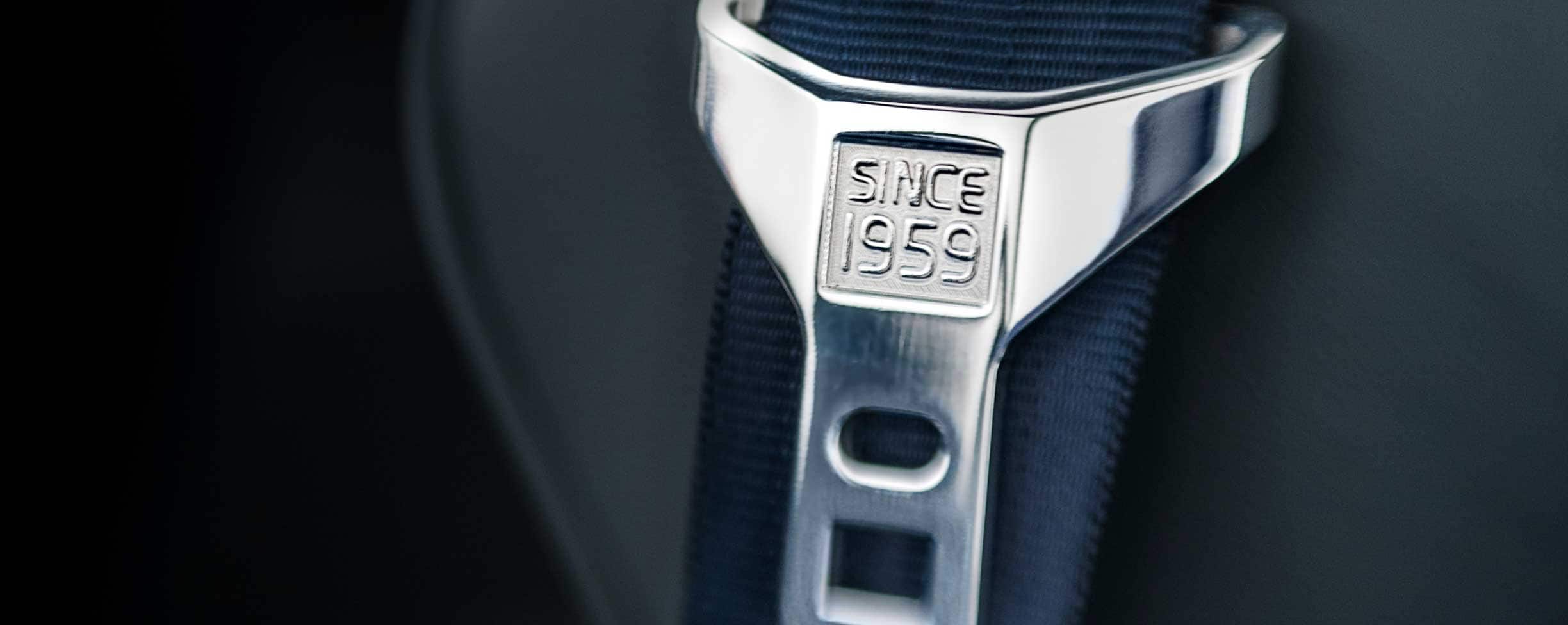 Um cinto de segurança em cinzento com o texto "Desde 1959" gravado na fivela.