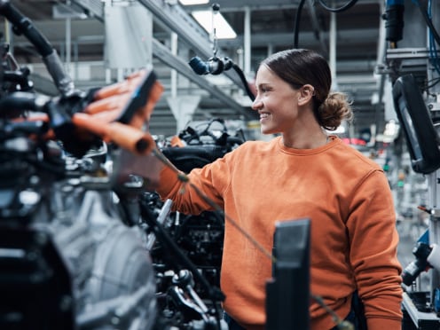 A smiling woman working on a car part inside a manufacturing plant.