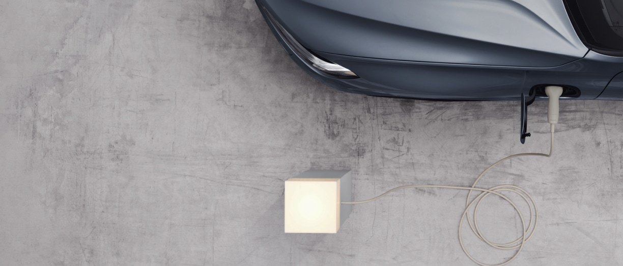 Top-down partial view of a Volvo charging from an outlet that’s lit up.