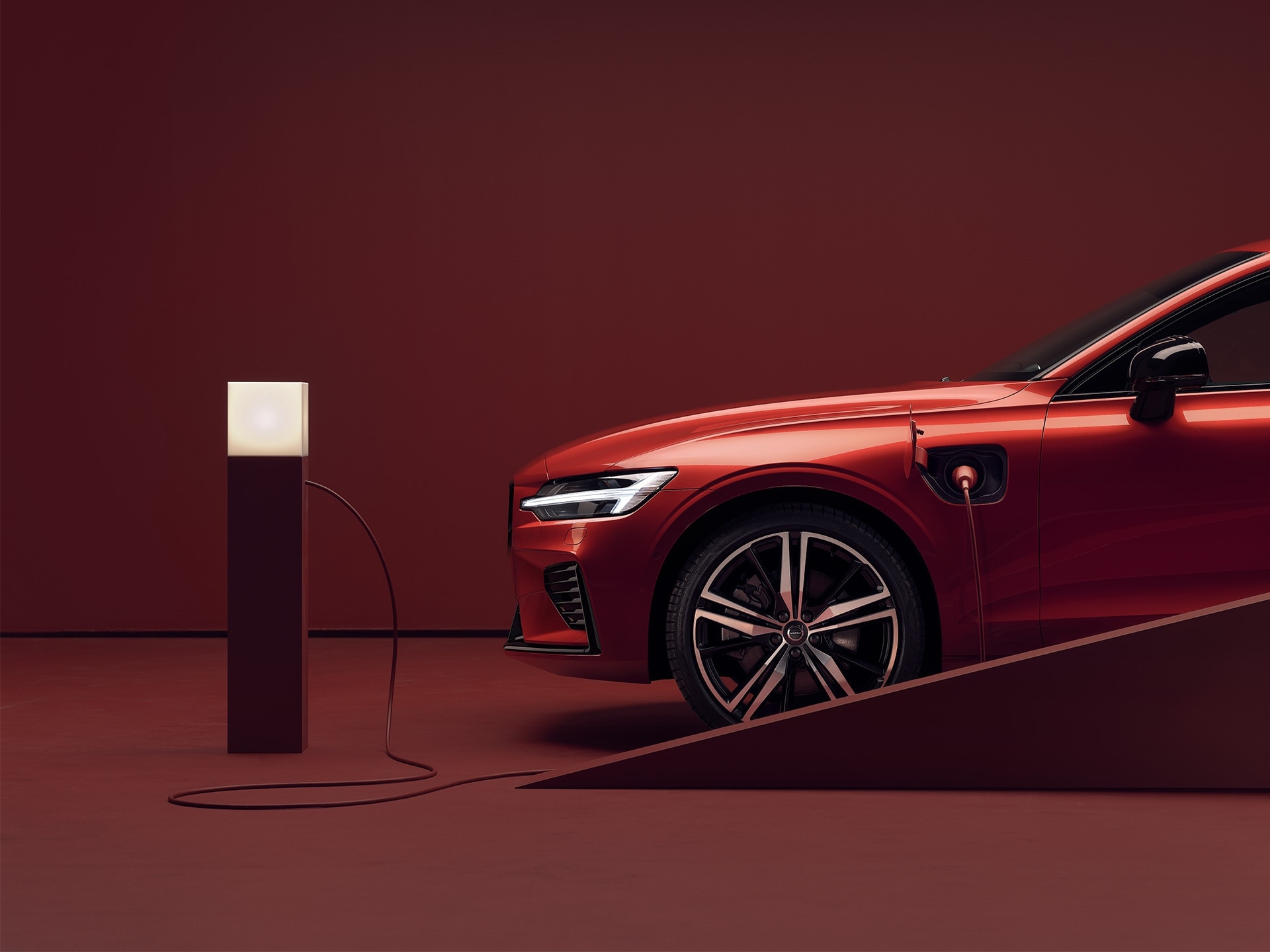 Une berline Volvo rouge en stationnement est branchée à une borne de recharge