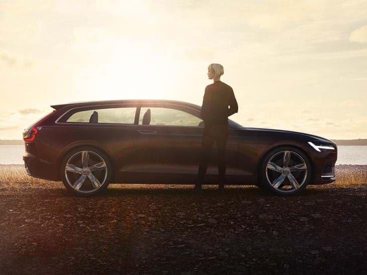 Una mujer de pie junto a un Concept Estate de Volvo recortado contra el atardecer