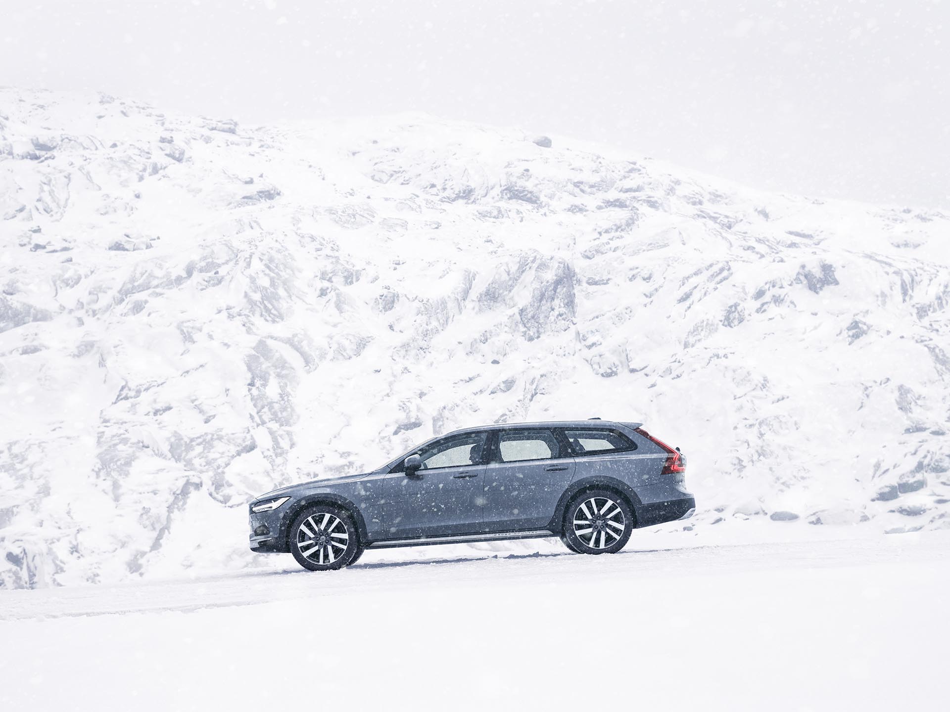 Karlı dağlarda seyreden midye mavisi bir Volvo V90 Cross Country Estate