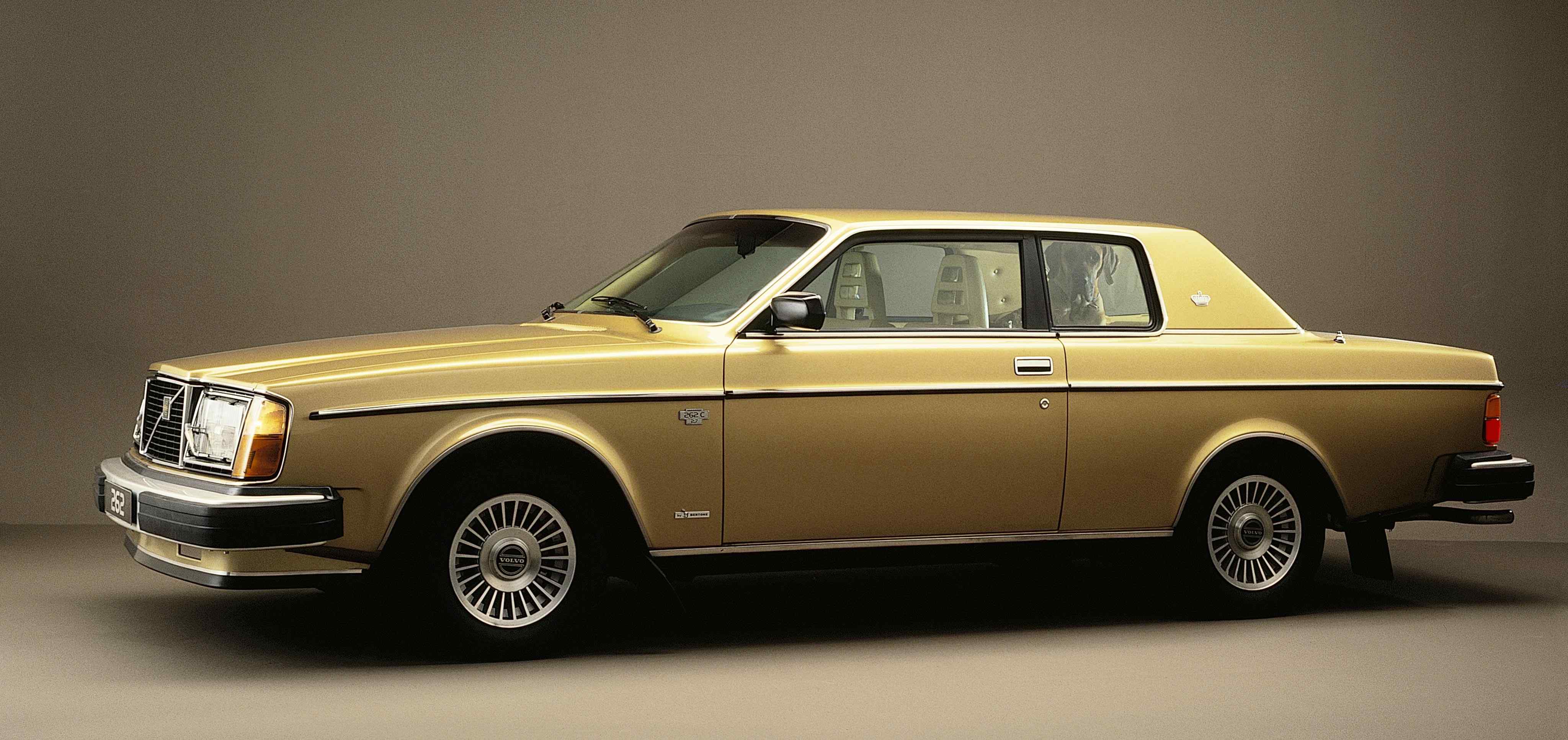 A gold Volvo 262C seen from side in studio environment