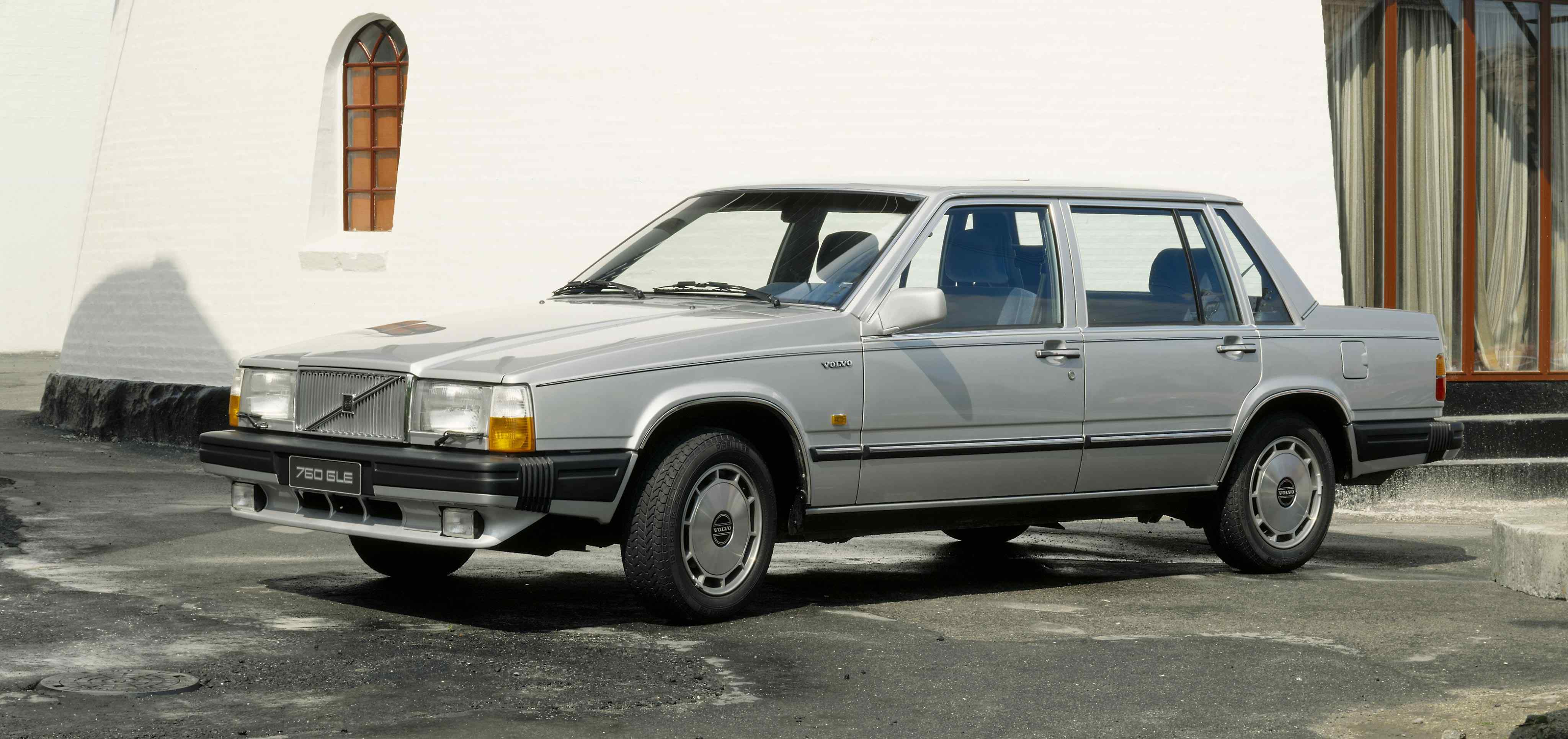 A silver Volvo 760 sedan parked in front of a white building