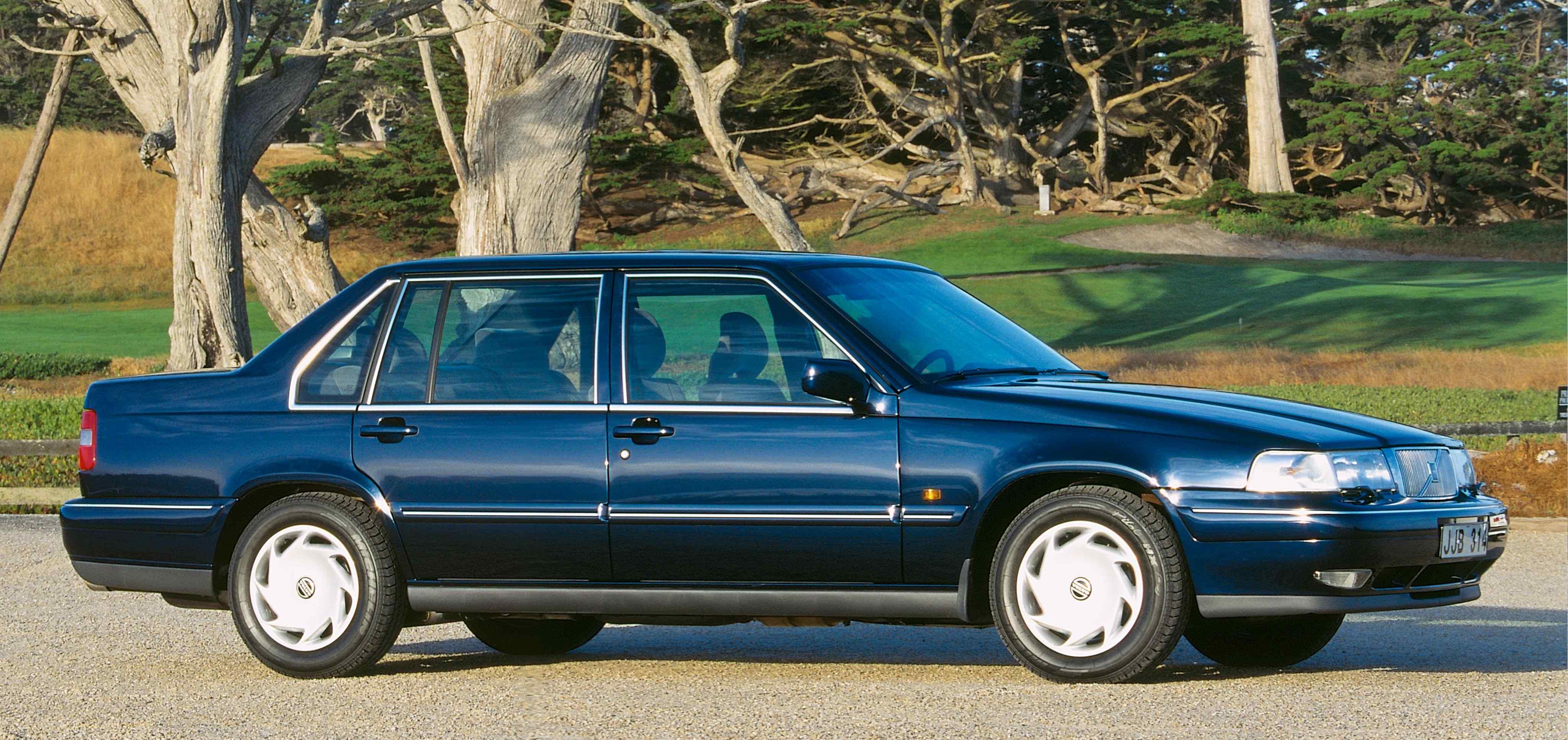 A blue Volvo 960 sedan parked in natural surroundings