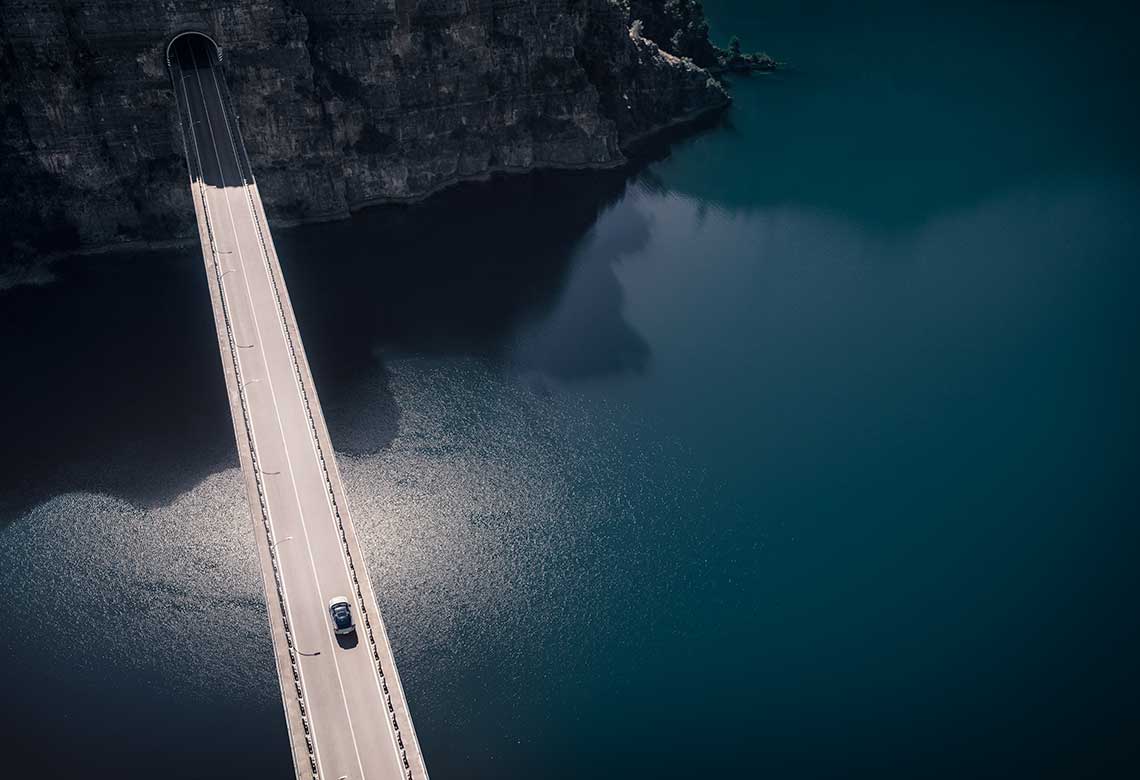 A Volvo car passing a bridge over water.