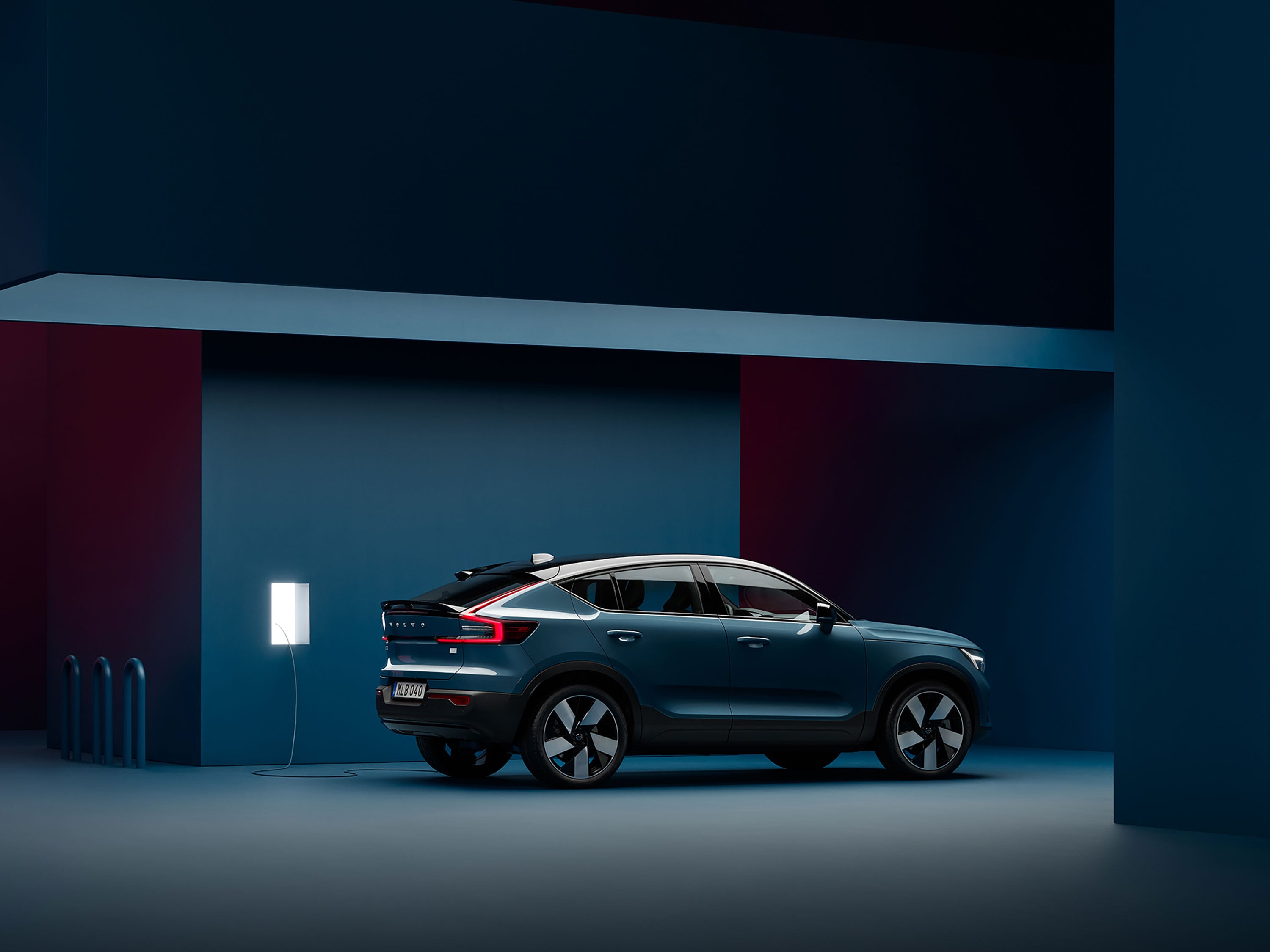 A Volvo C40 Recharge is parked in a dark blue room next to a charging station.
