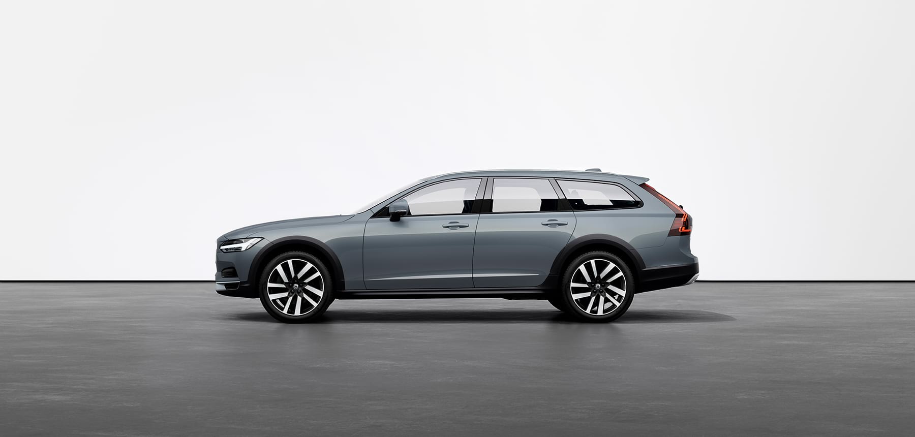 A mussel blue Volvo V90 Cross Country Estate standing still on grey floor in a studio