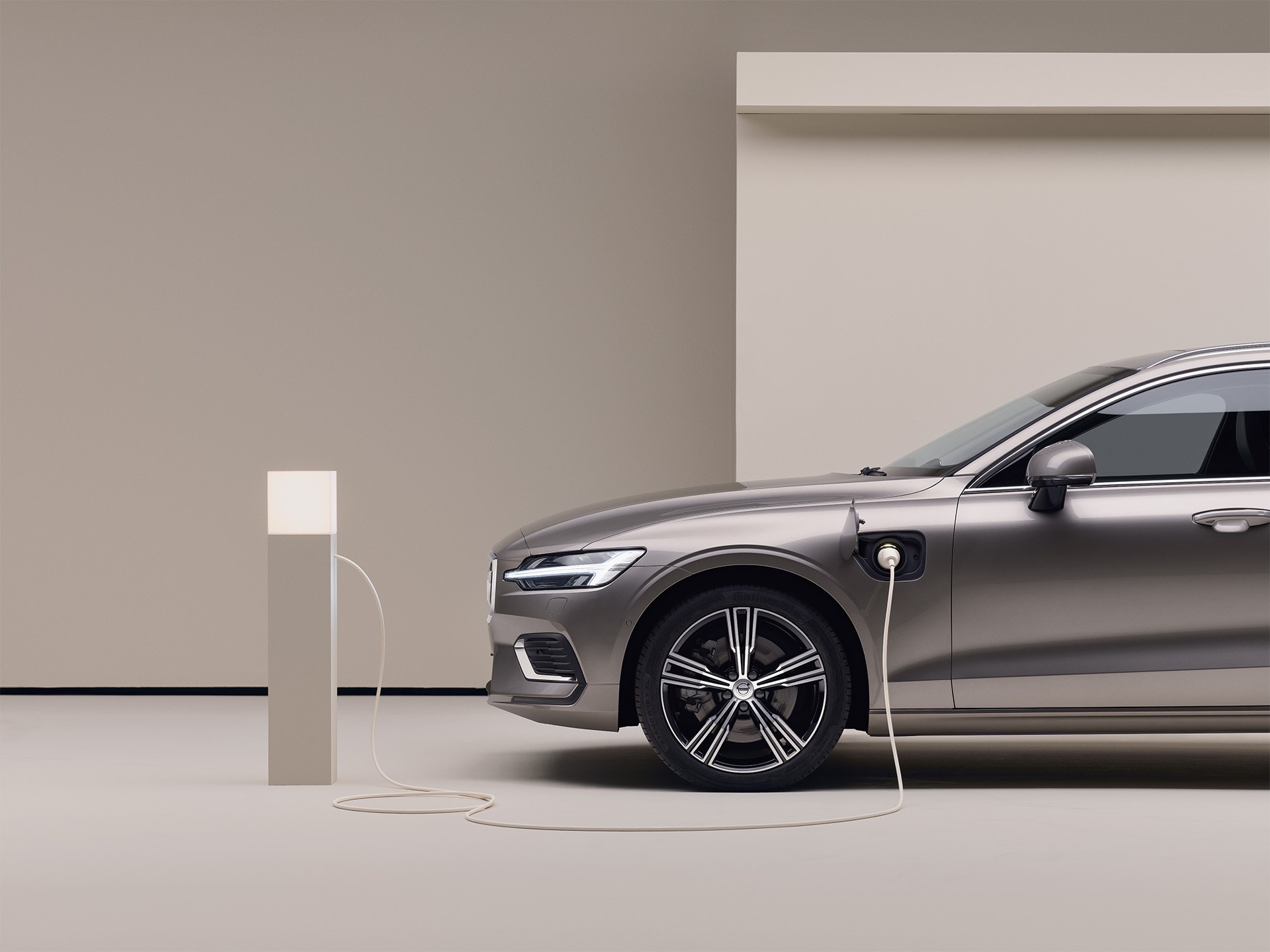 Stāvvietā novietots pelēkas krāsas Volvo universālis, pievienots uzlādes punktam