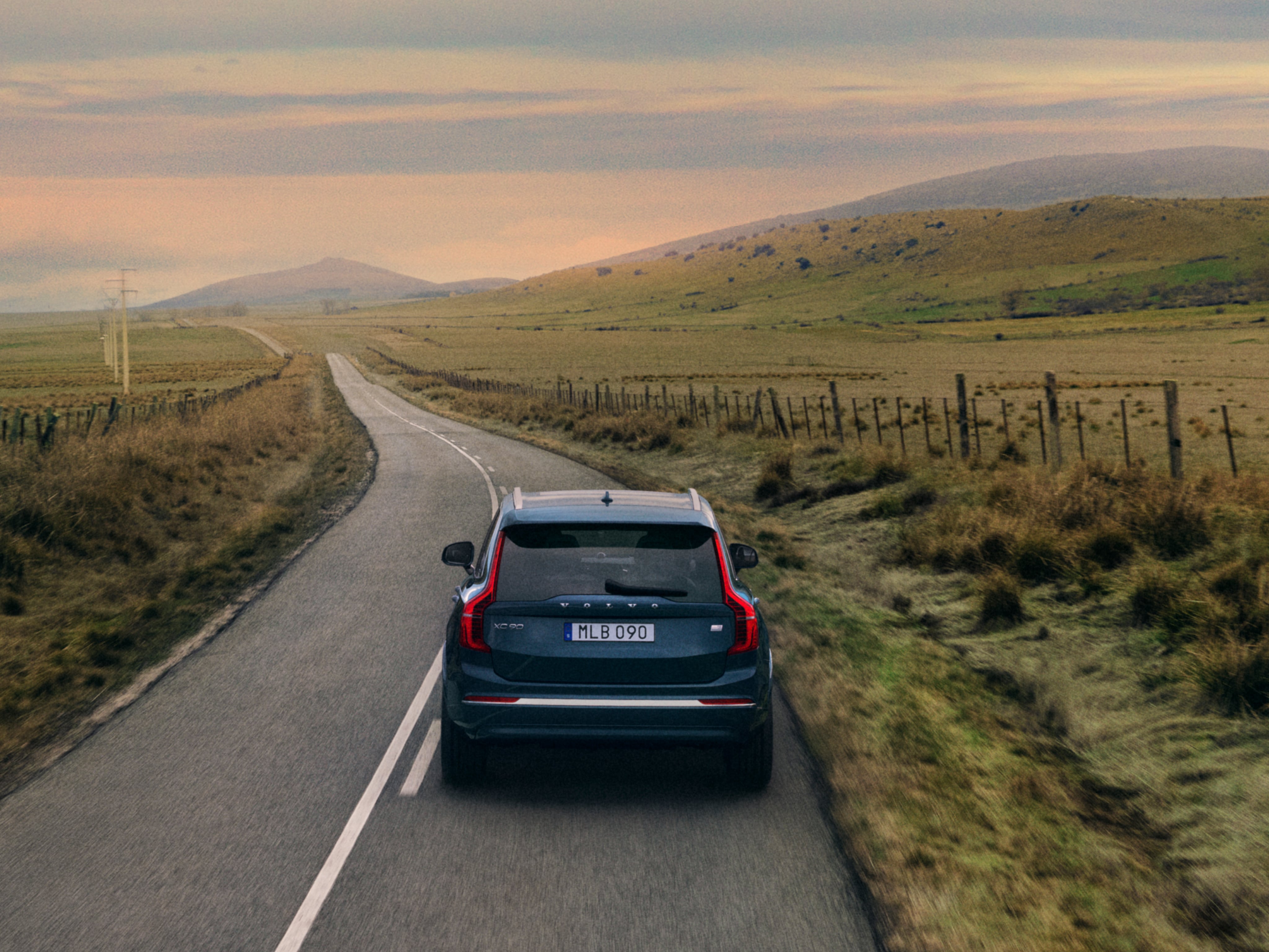 Un Volvo XC90 Recharge hybride rechargeable vu de derrière sur une route de campagne.