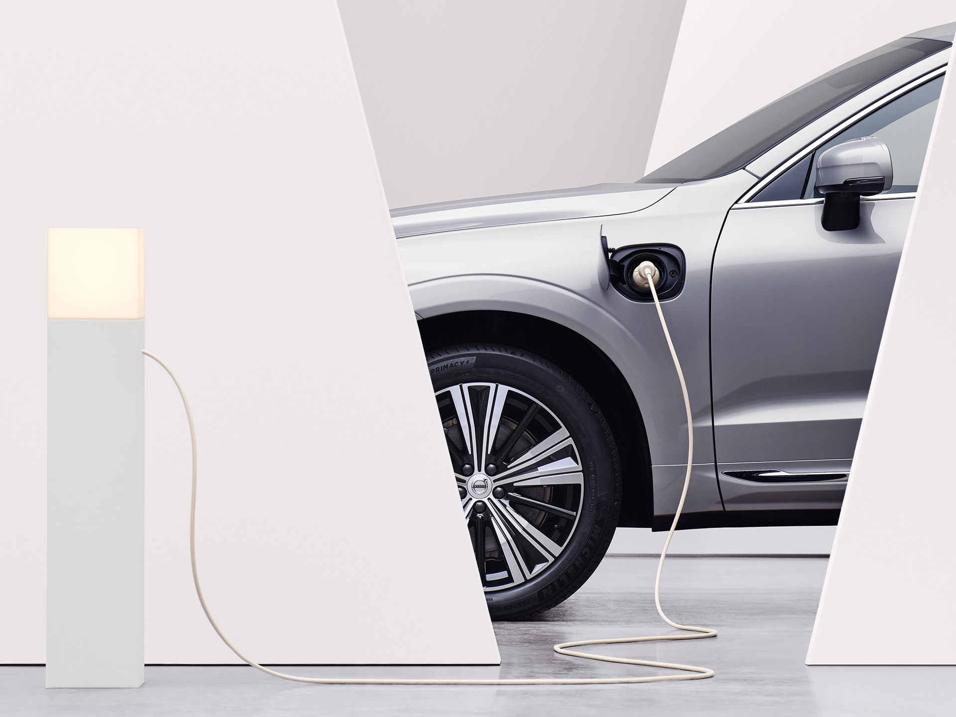 A parked luminous silver Volvo SUV is plugged into a charging point