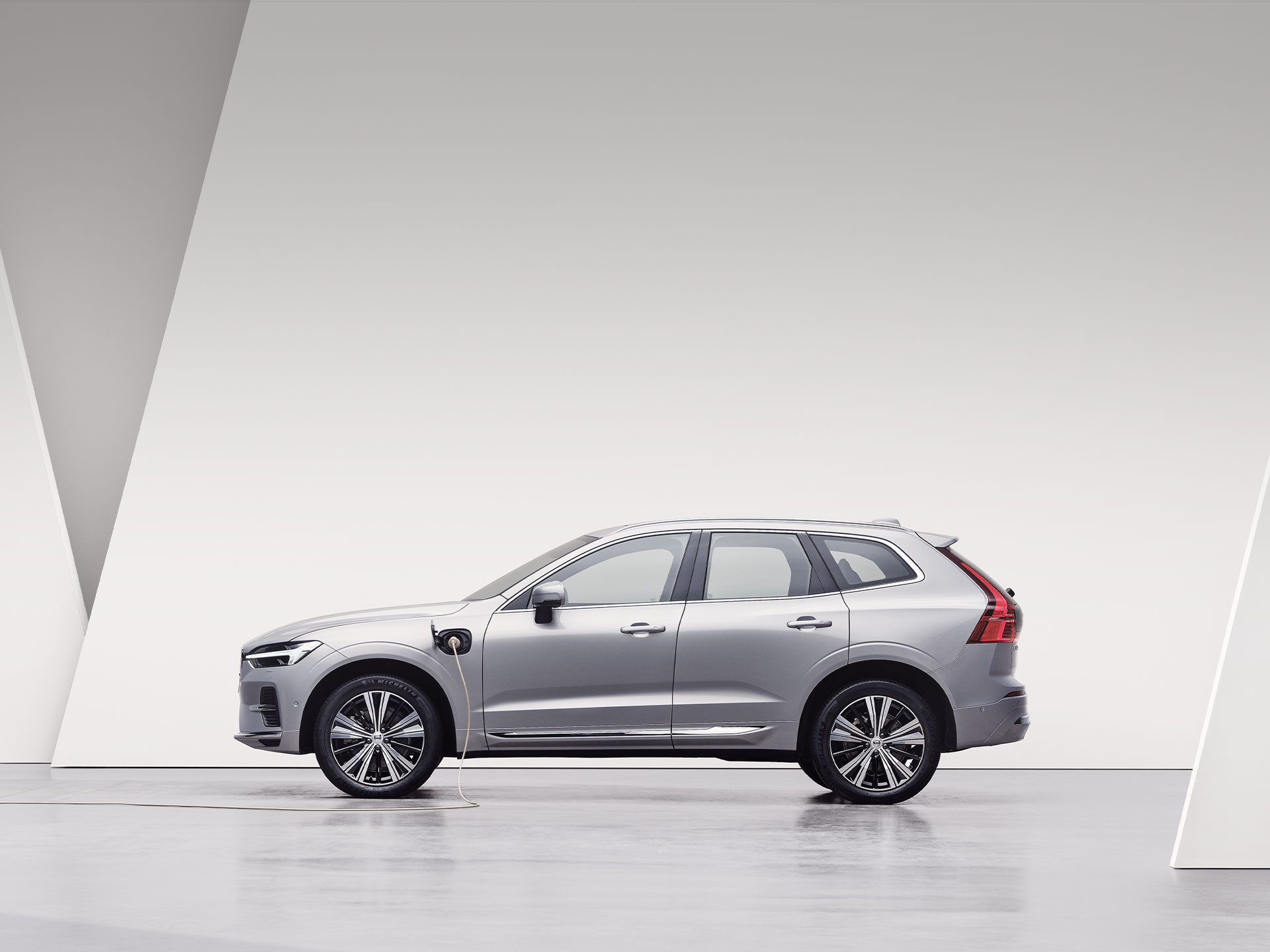 A silver Volvo XC60 Recharge, charging in white surroundings.