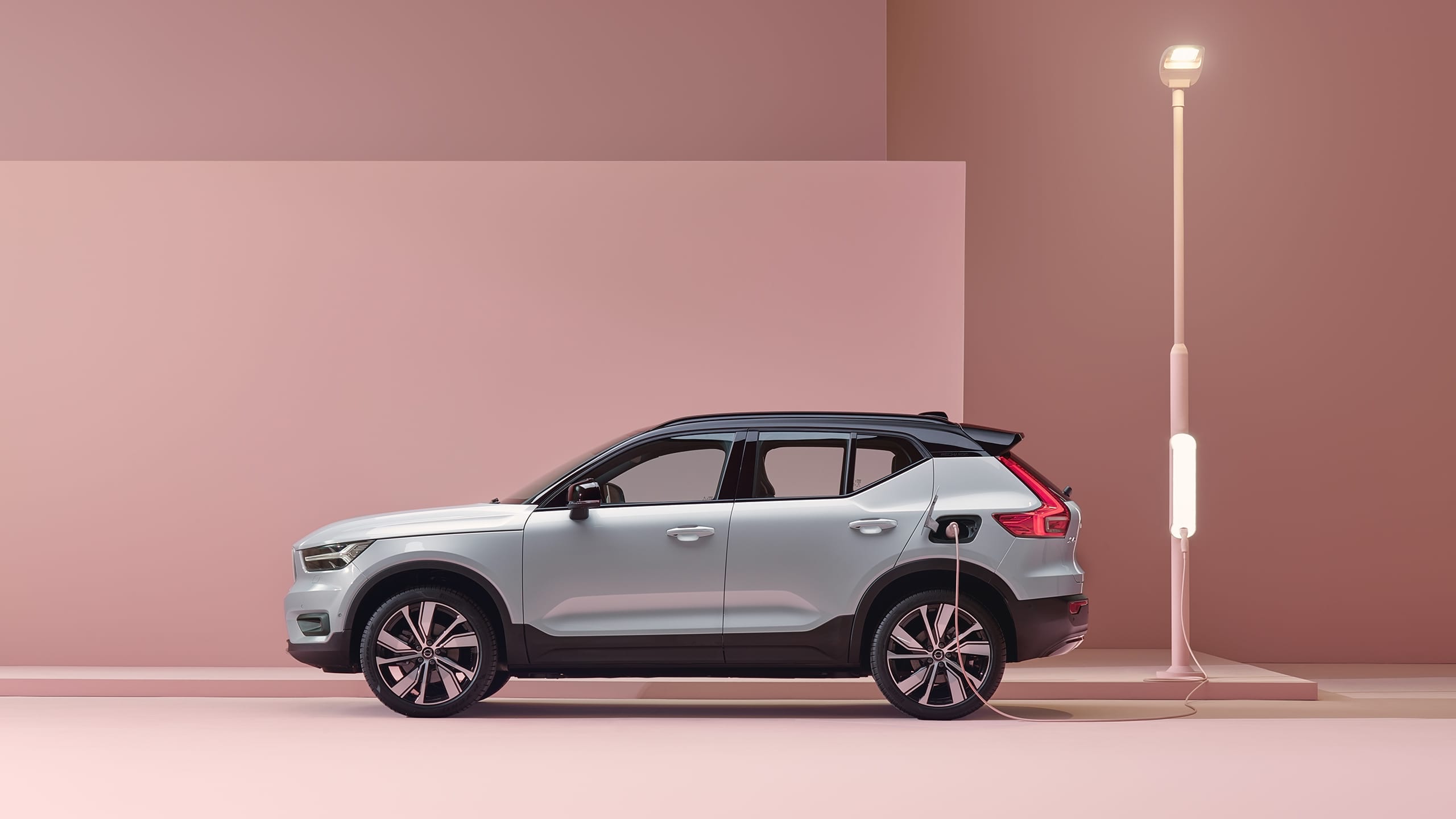 A grey Volvo XC40 full electric SUV being charged in a pink city