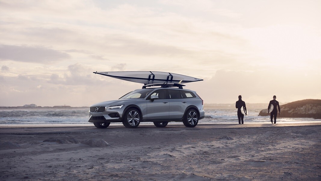 A V60 Cross Country with a kayak on the roof is parked on a beach.
