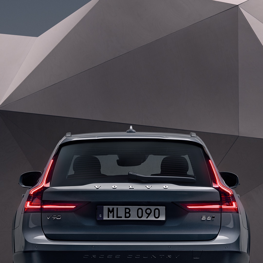 The rear exterior of a mussel blue metallic V90 Cross Country standing in front of an artistic wall.