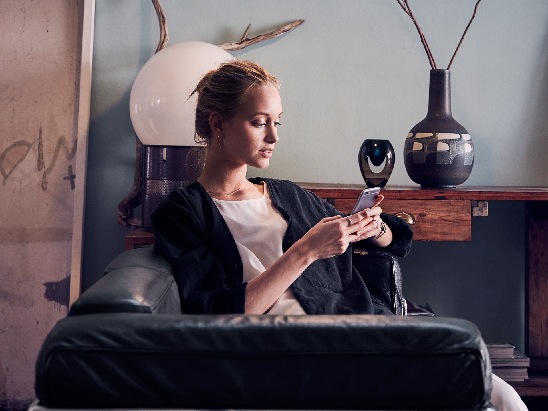 Una chica rubia sentada en un sofá utilizando la aplicación de Volvo Cars en su teléfono.