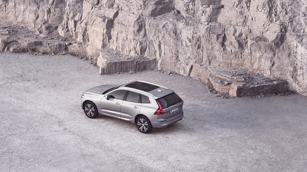 A silver Volvo XC60 with a panoramic roof next to a rock wall.