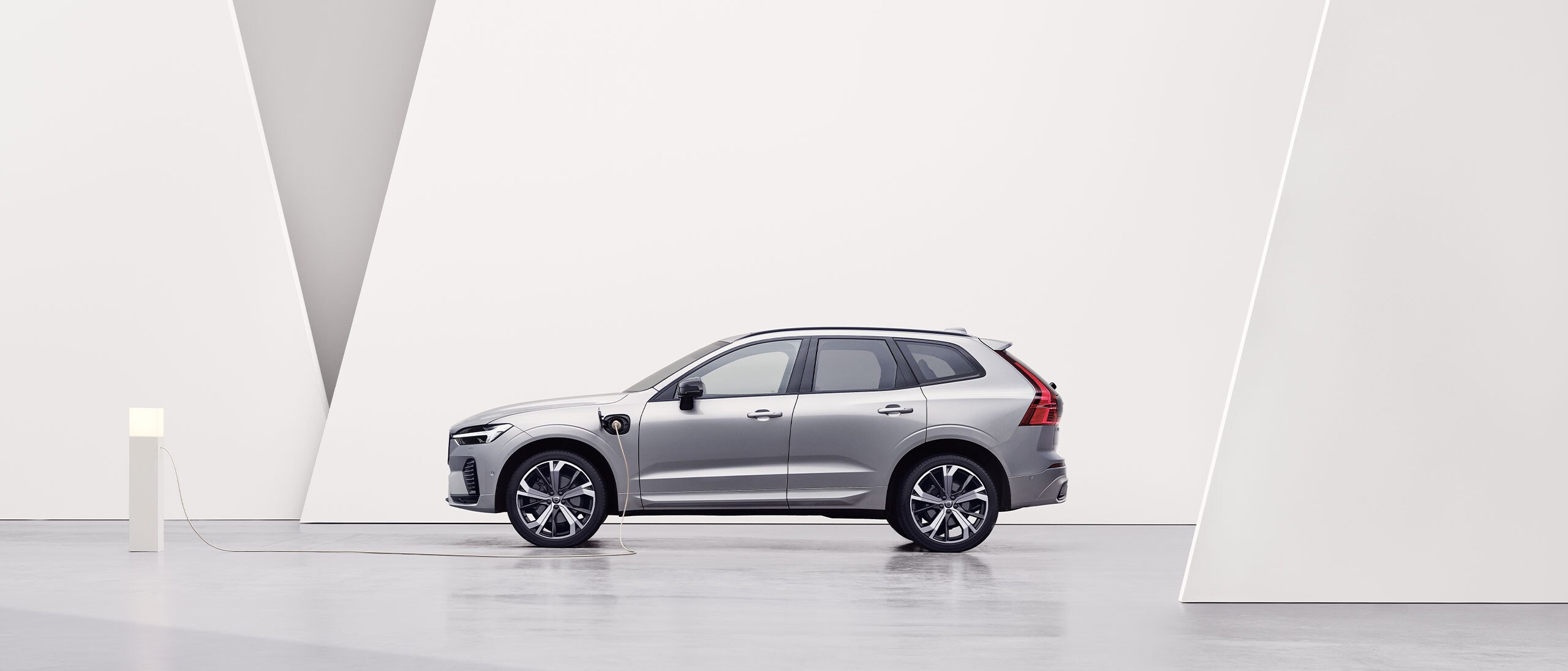 A silver Volvo XC60 Recharge, charging in white surroundings.