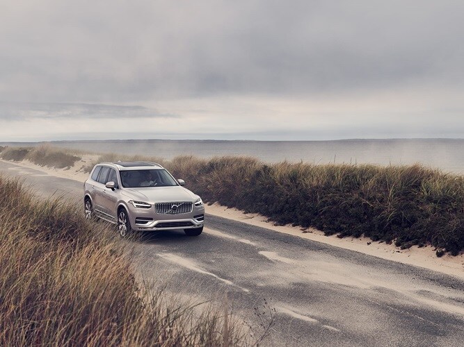 Volvo XC90 едет вдоль береговой линии по небольшой песчаной дороге.