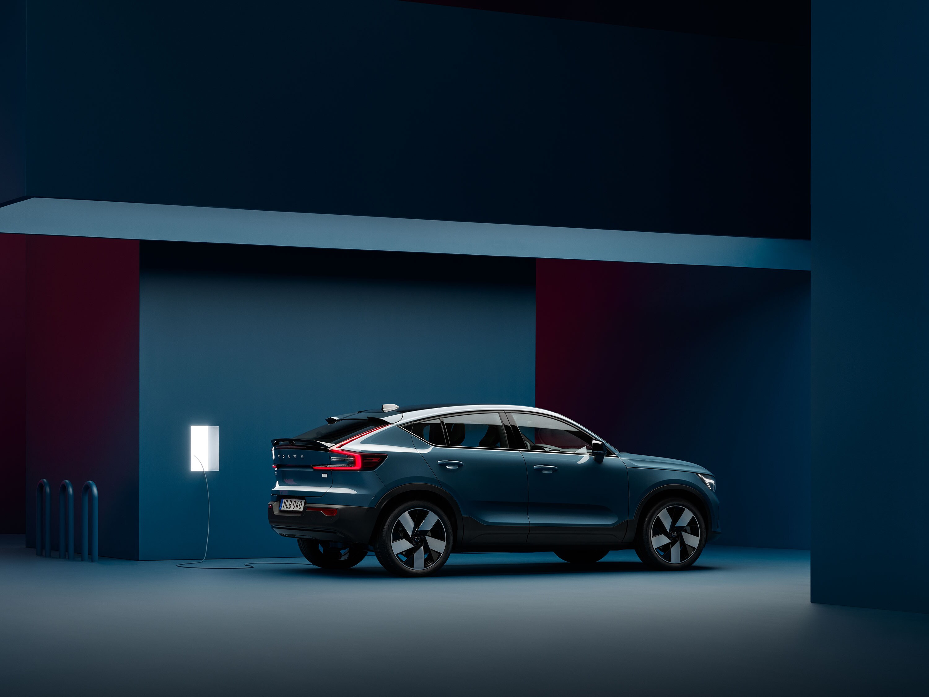 A Volvo C40 Recharge is parked in a dark blue room next to a charging station.