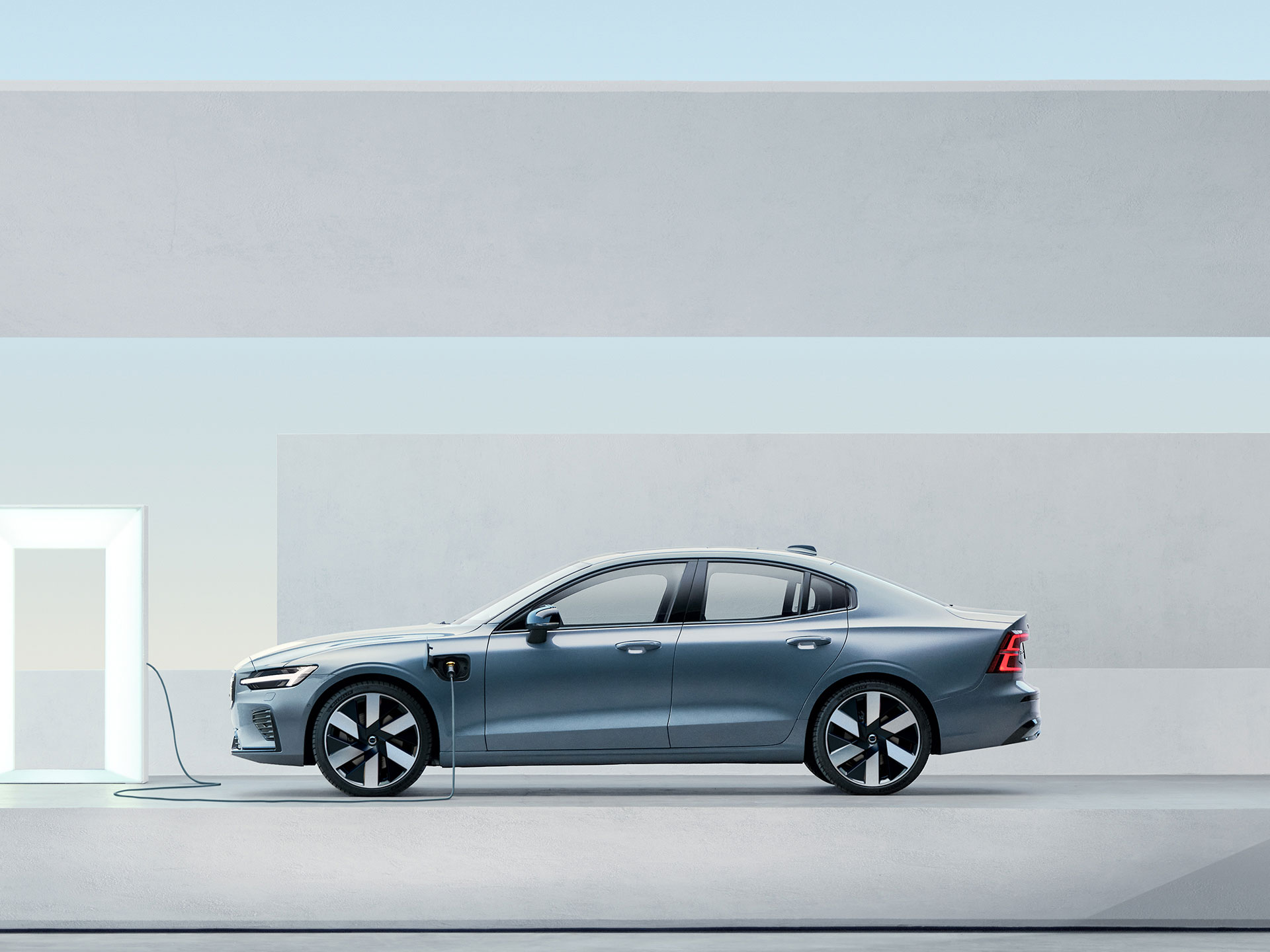 A Volvo Sedan Recharge parked outside in front of a big wall