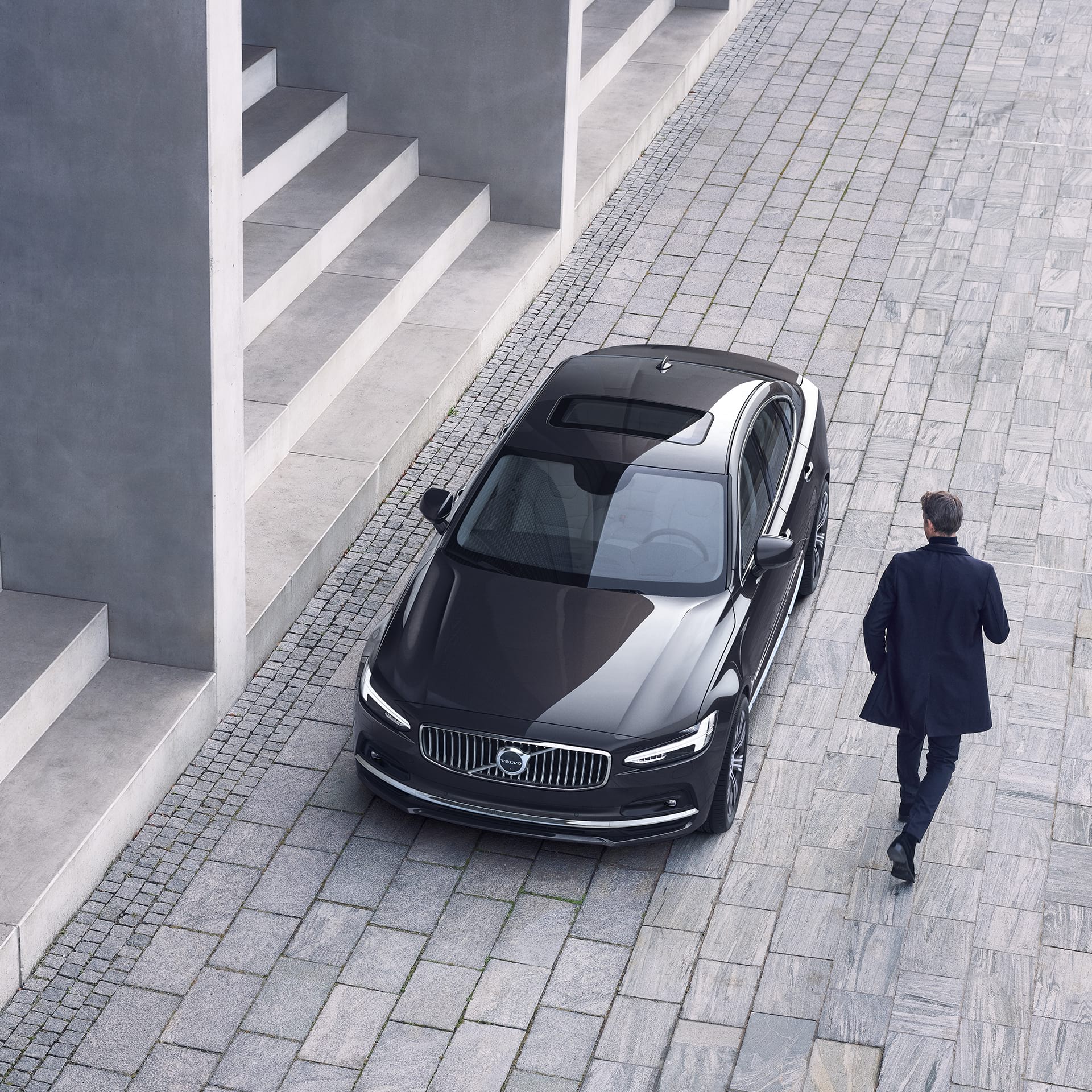 A Volvo S90 is parked in front of a set of stairs, a man walks towards the car