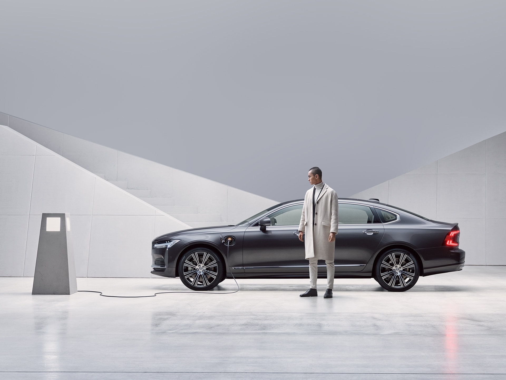 A man is standing in front of his grey Volvo S90 Recharge, being charged