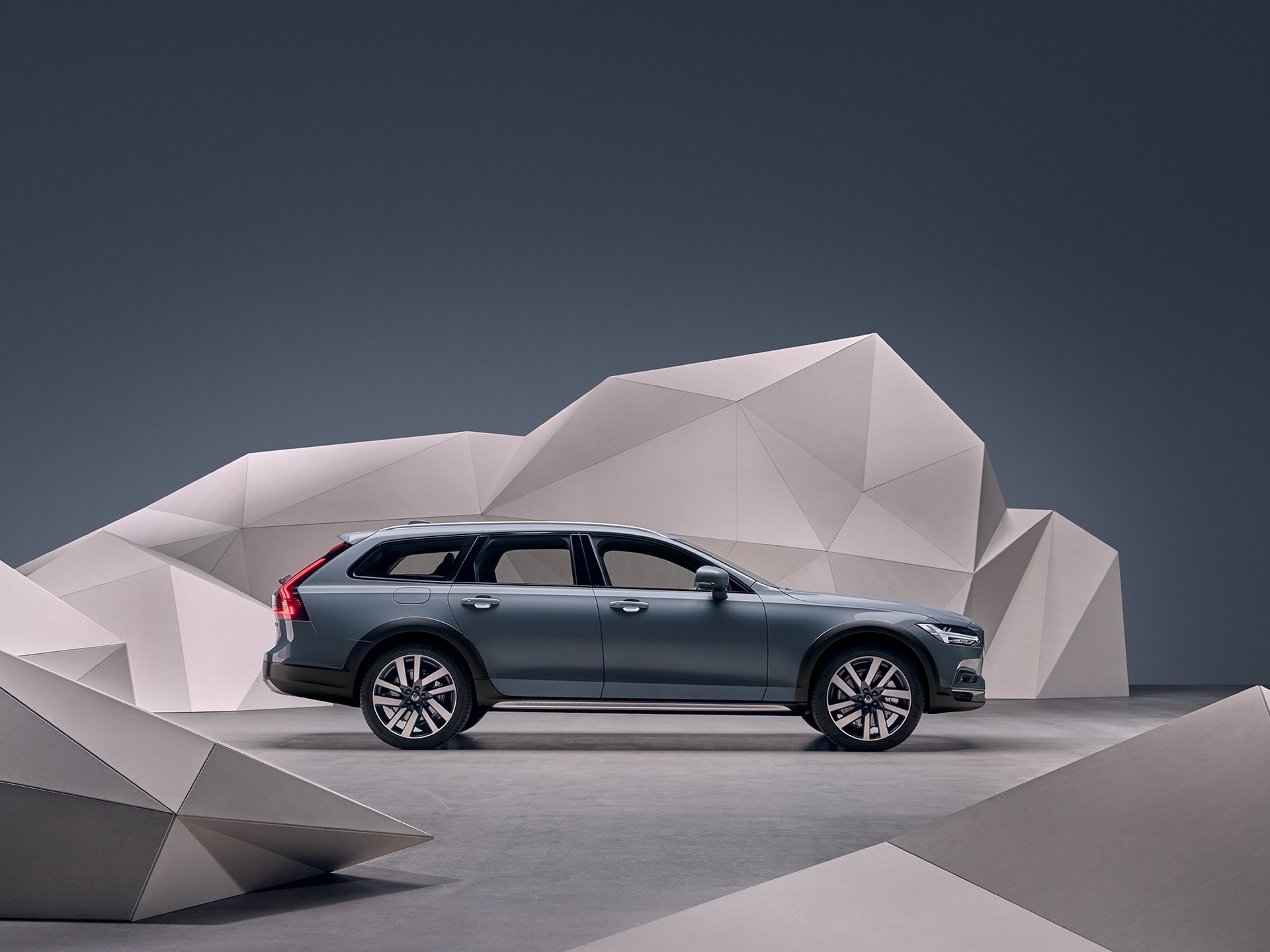 A mussel blue metallic Volvo V90 Cross Country standing in front of an artistic wall