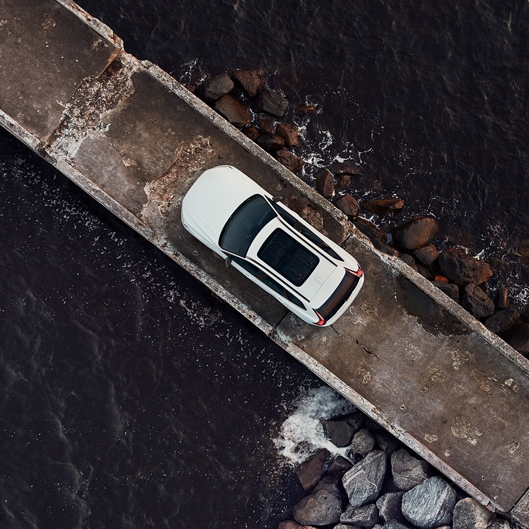 A white Volvo XC60 Recharge is parked on a barge surrounded by the sea