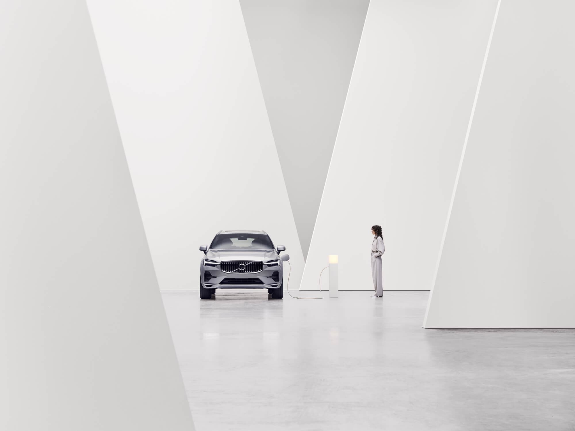 Un Volvo junto a un poste de recarga visto desde el frente con un entorno interior en blanco