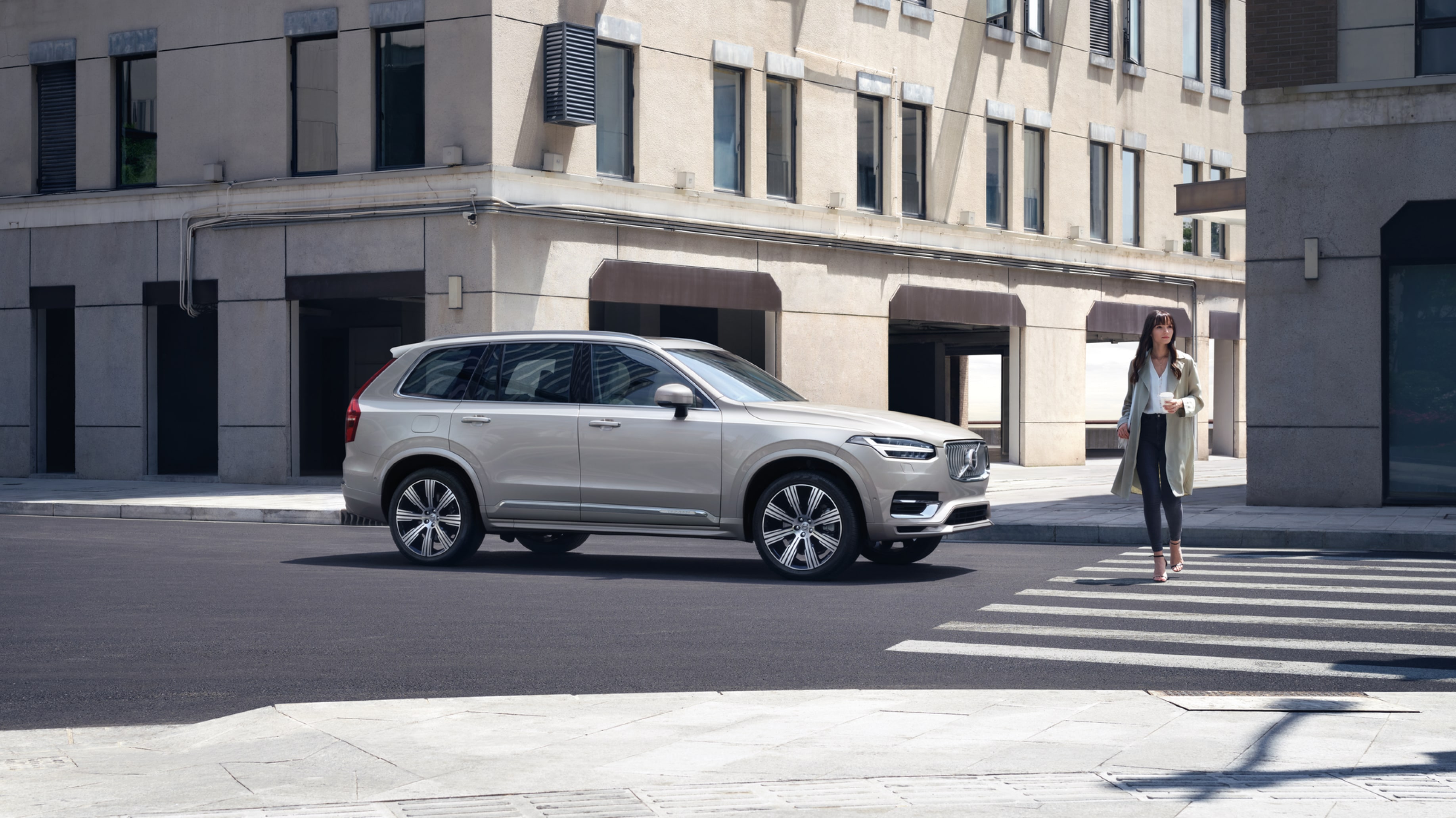 A Volvo XC90 stops at a zebra crossing while a lady with a coffee cup in hand cross.