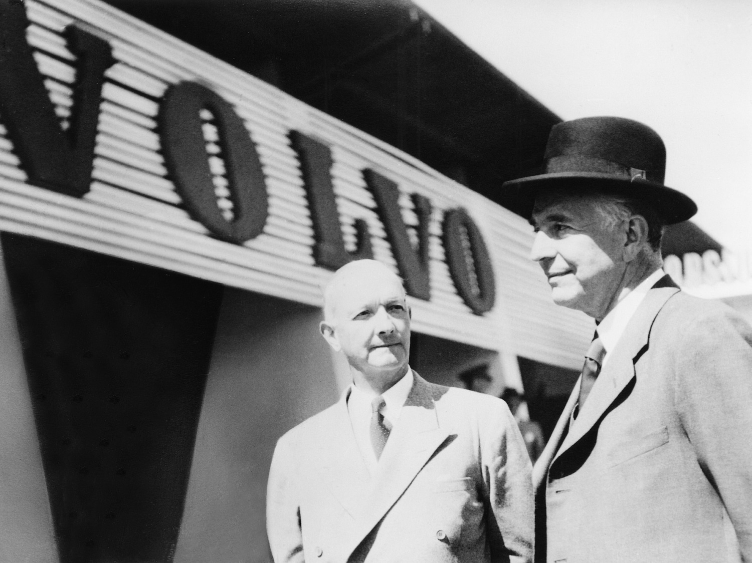 A vintage shot of two gentlemen standing beside a VOLVO signboard.