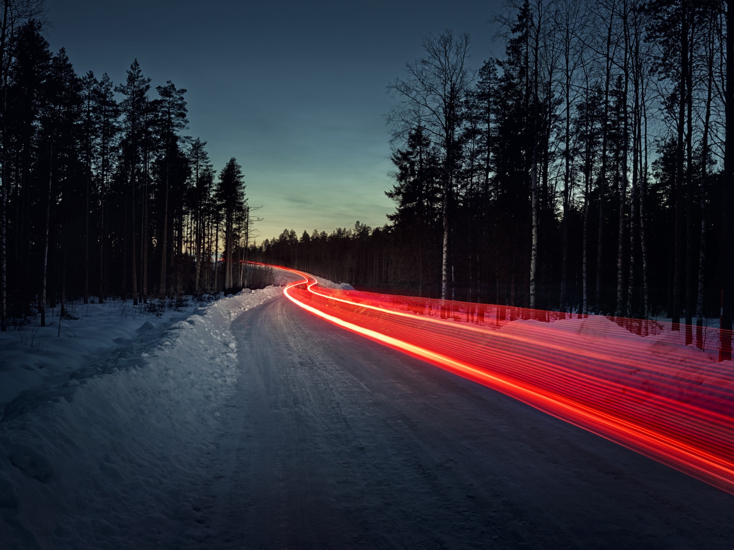 凍結路を走行するクルマのテールライトが発する赤い光の軌跡を長時間露光で捉えた画像。