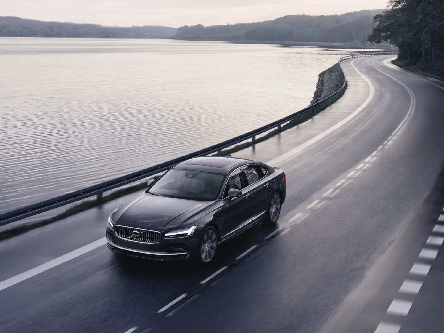 Автомобиль Volvo едет по дороге, граничащей с озером.