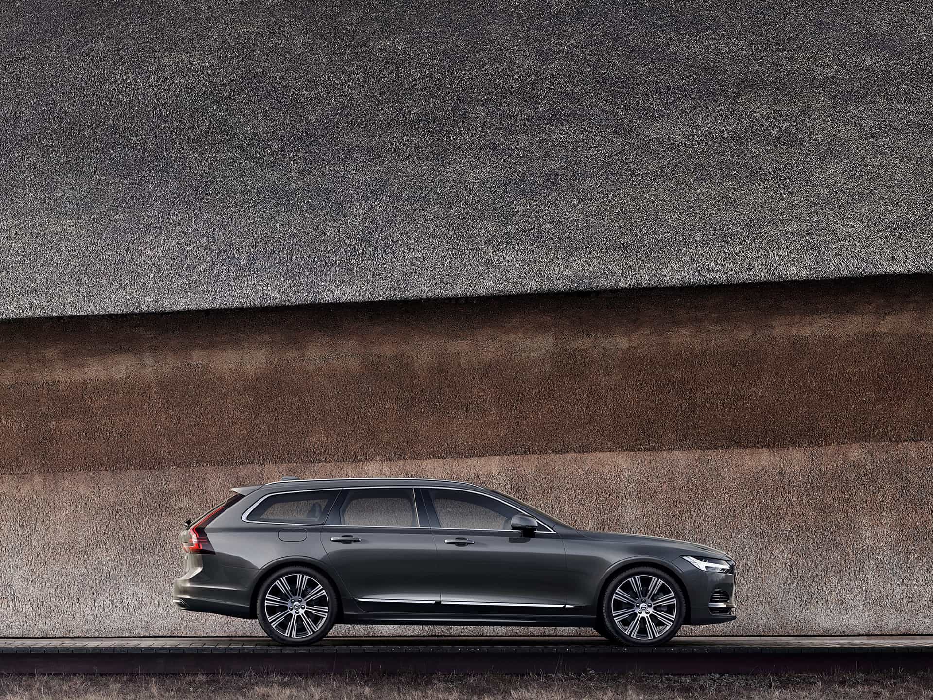A dark grey Volvo V90 parked against a wall.