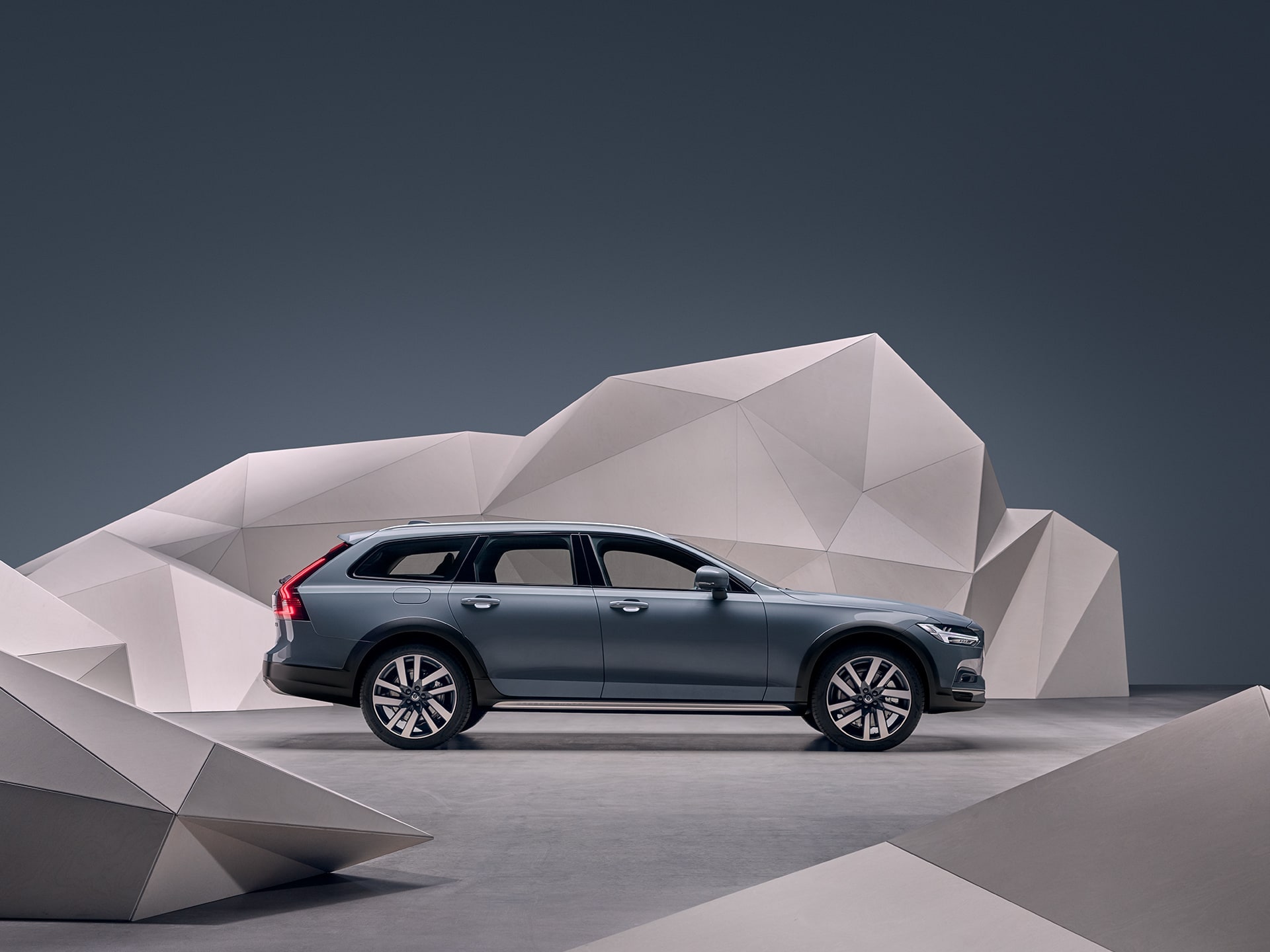 A mussel blue metallic Volvo V90 Cross Country standing in front of an artistic wall.