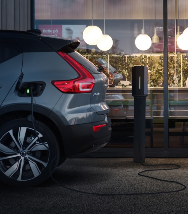Partial rear view of a charging XC40 parked outside a cafe where two people are sat facing each other.