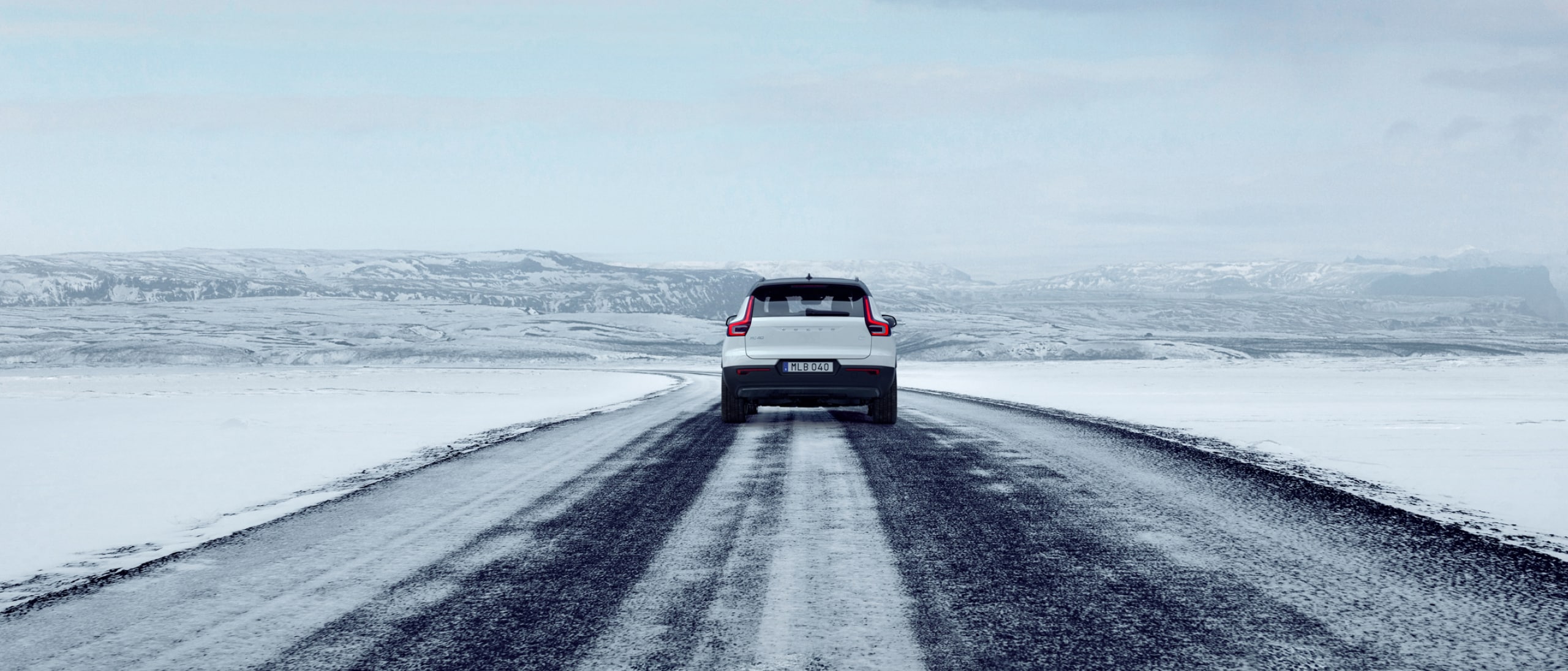 Rear view of a white Volvo XC40 driving on an icy road.