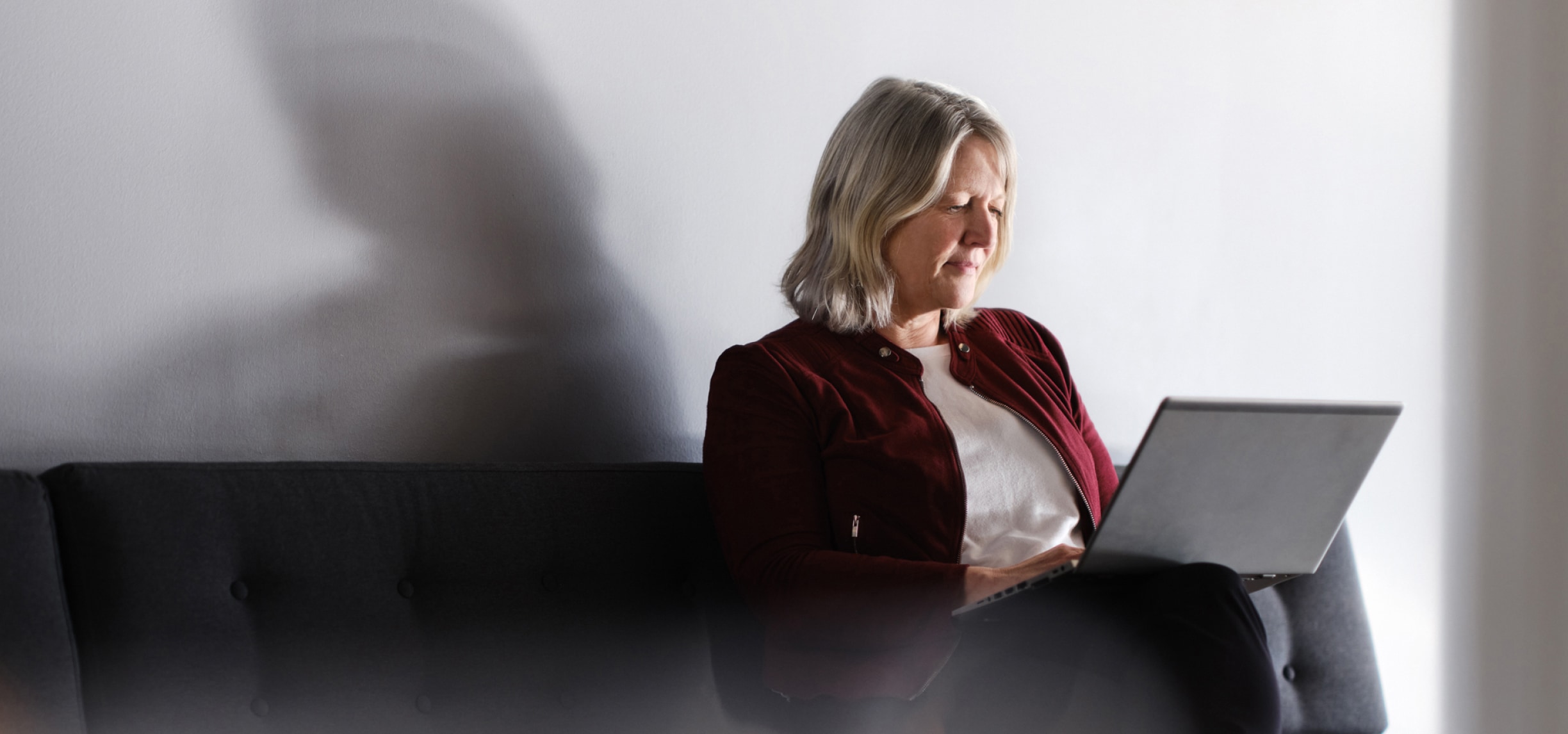 Una donna seduta su un divano nero mentre usa un portatile